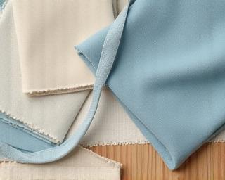 Mood-board collage showcasing soft blue fabrics, sandy beige wallpapers, and natural wood samples